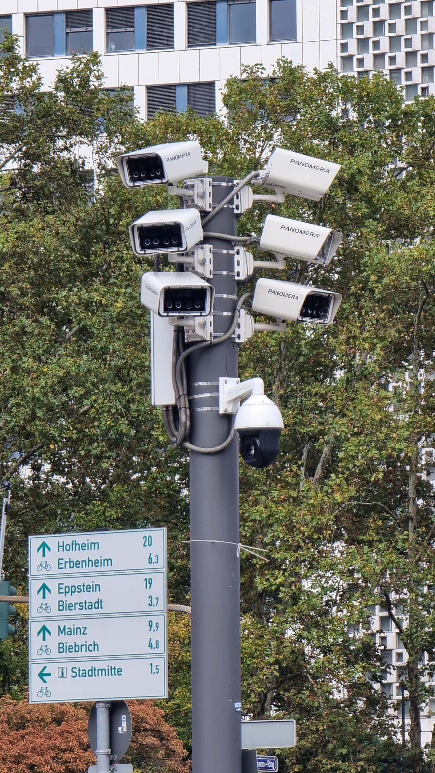 Six box surveillance cameras and a dome camera mounted on a pole above a street direction sign