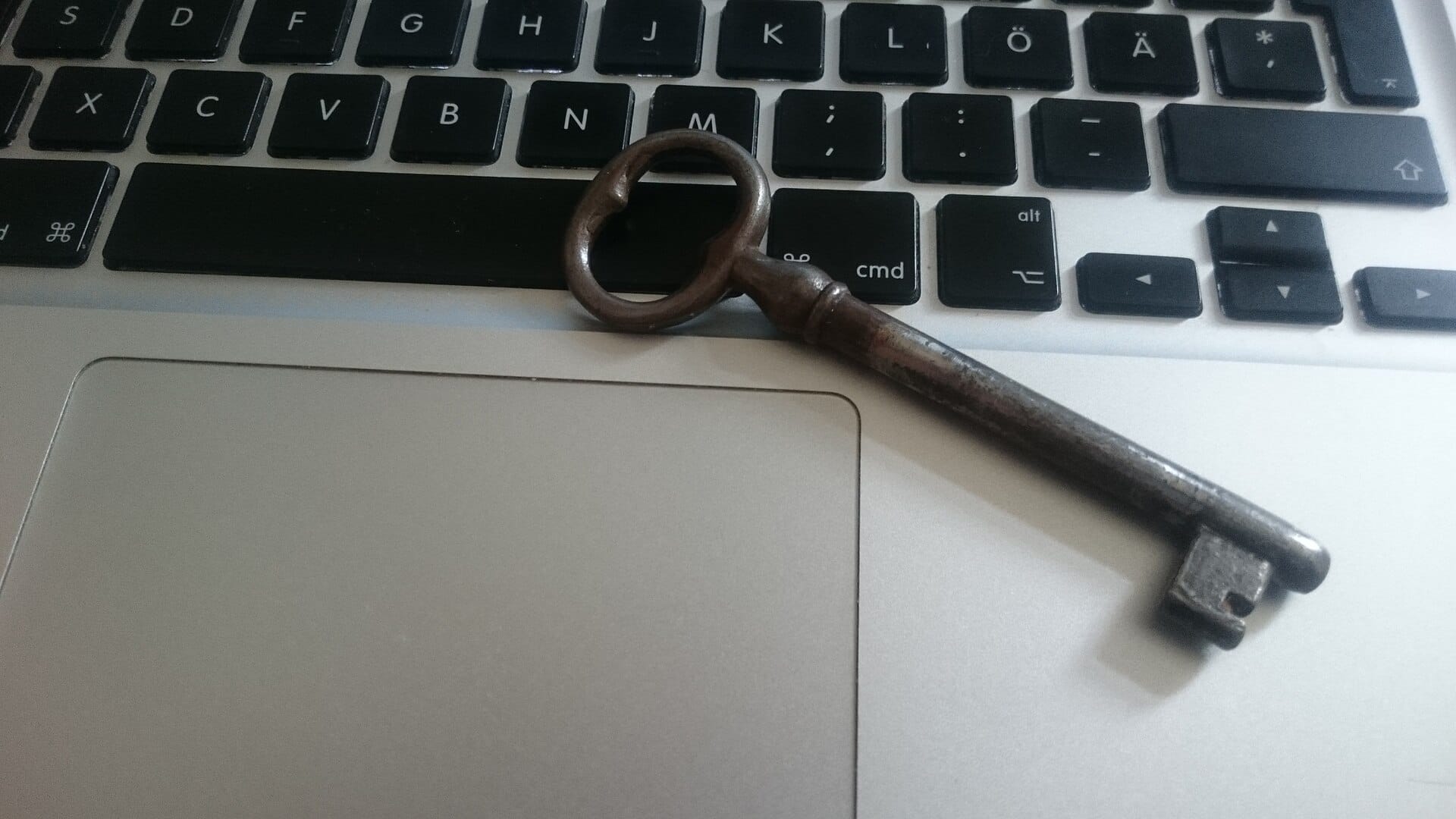 Old metal key lying across a laptop keyboard, a symbol of the passwords attackers try to crack