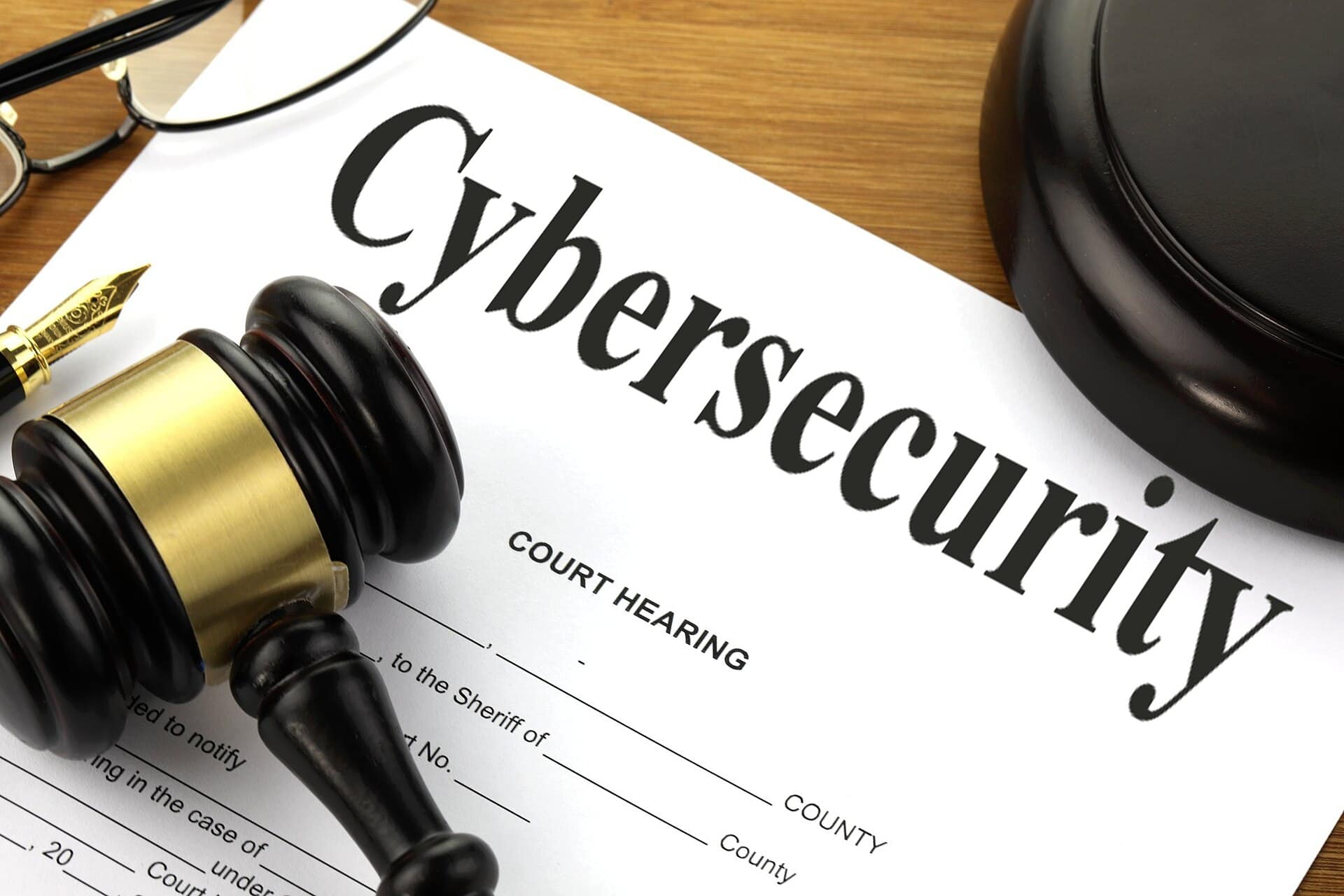 A gavel and reading glasses on a court hearing document titled Cybersecurity, a symbol of the law around hacking