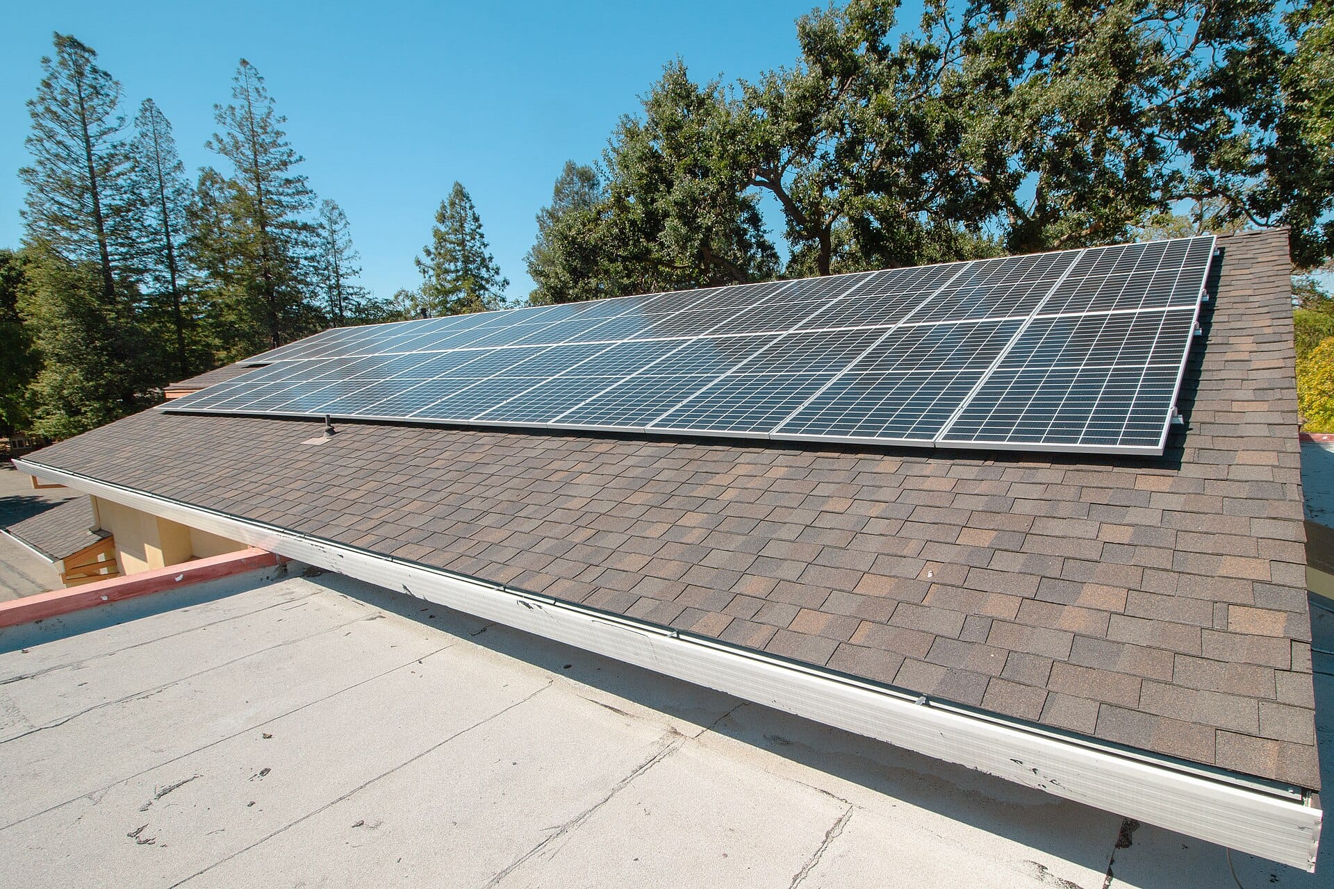 Photovoltaic panels mounted in rows on a tiled church roof under a blue sky