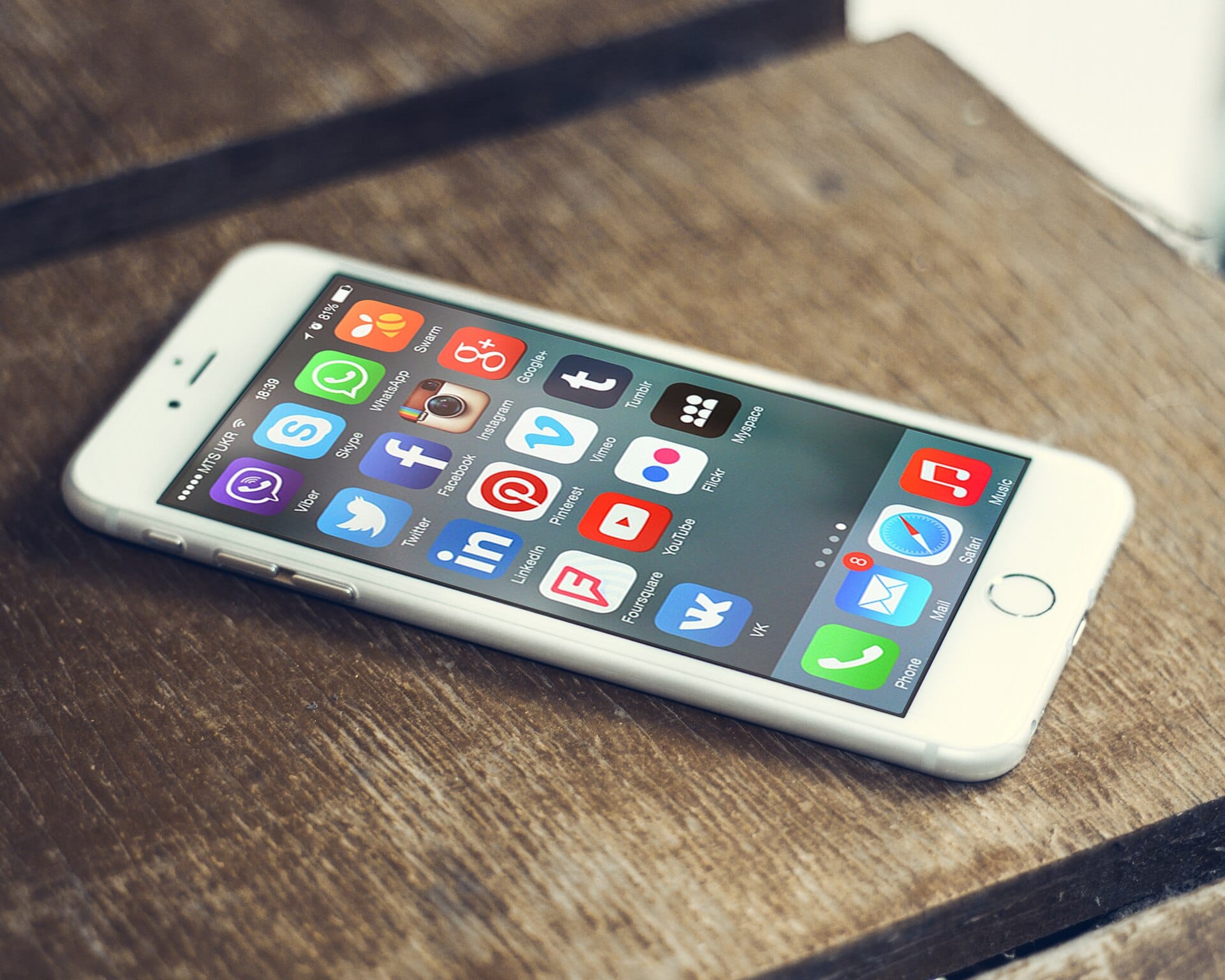 iPhone lying on a wooden table with social media app icons filling the screen