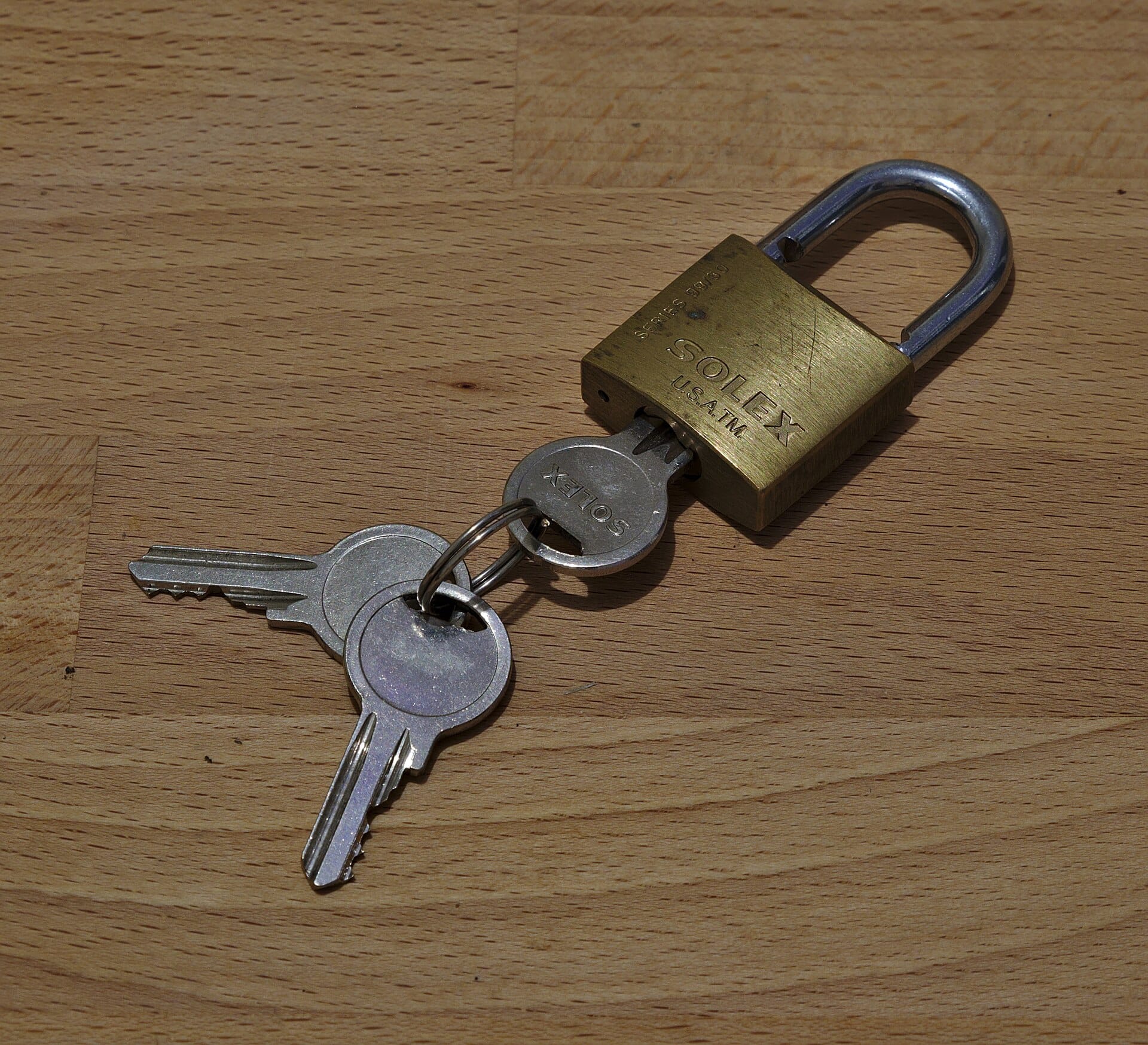 A brass padlock and keys resting on a wooden surface