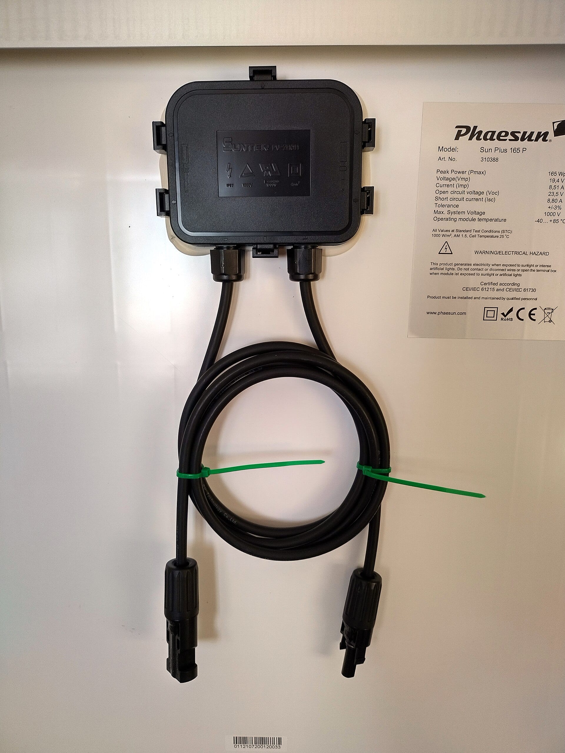 Rear of a solar panel showing its junction box, coiled cables and the maker's label with ratings and CE marks