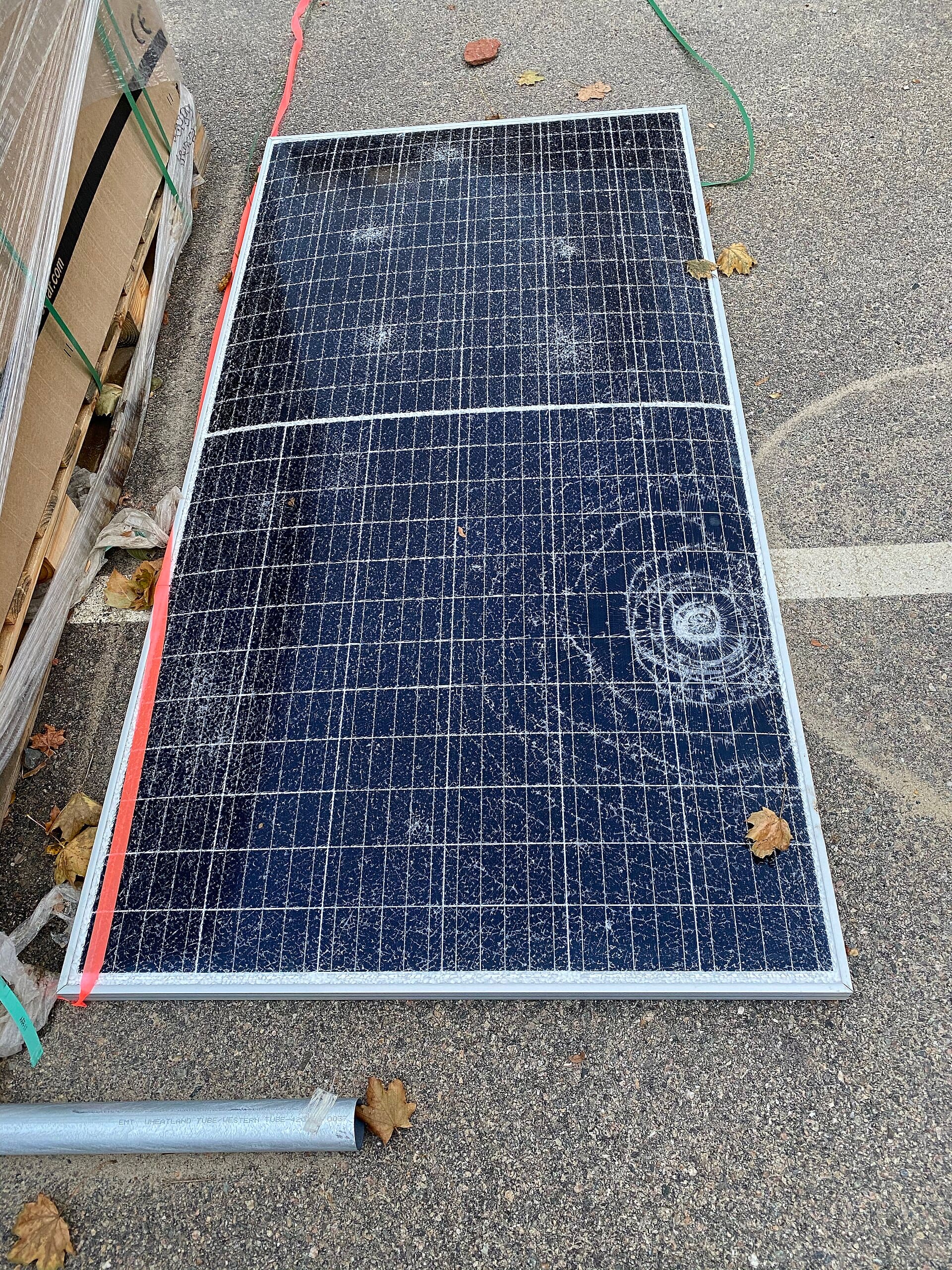 Discarded solar panel with a circular impact crack and a long fracture running across the cell surface