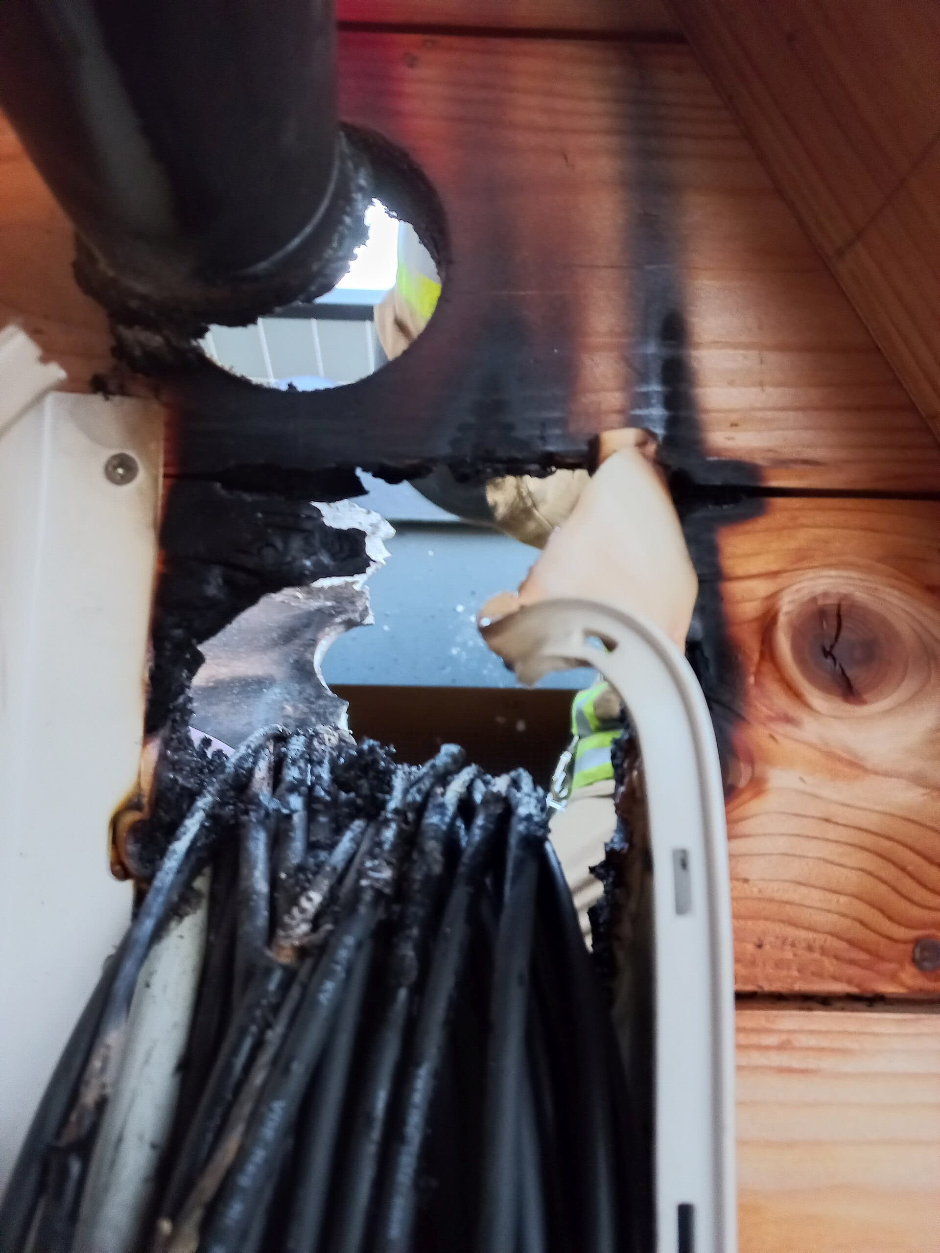 Charred solar DC cables melted through at a roof penetration, soot staining the timber above
