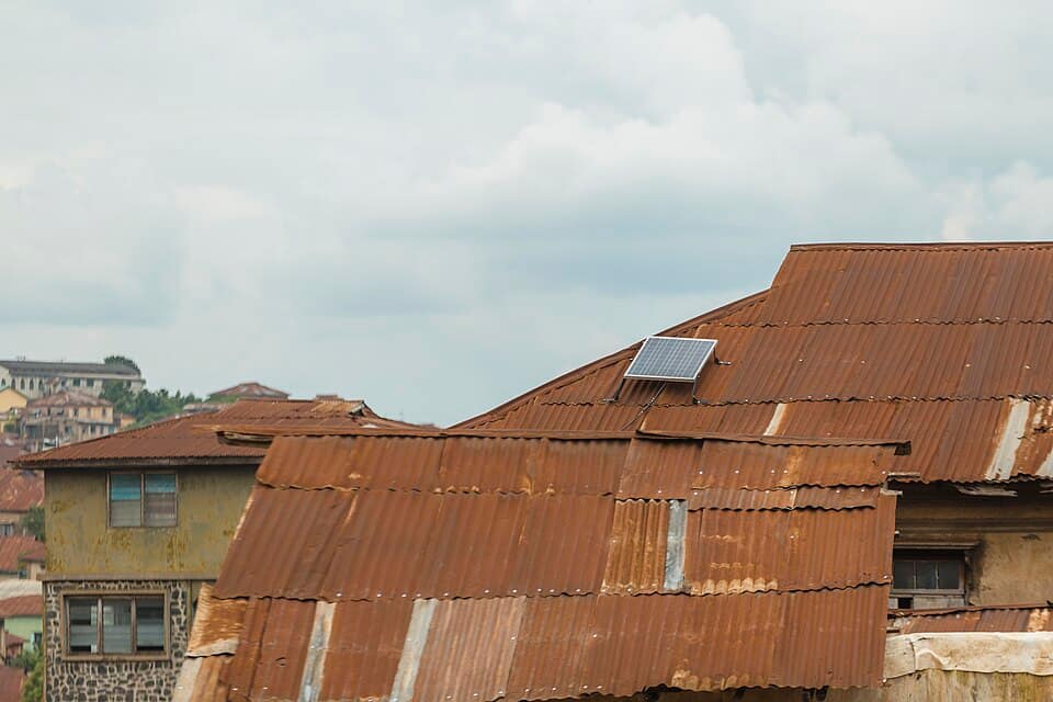 Small solar panel on a rusted corrugated-iron roof in Abeokuta under heavy grey rain clouds