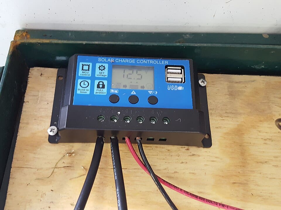 Blue solar charge controller with an LCD reading 12.5 volts and cables running into its terminals